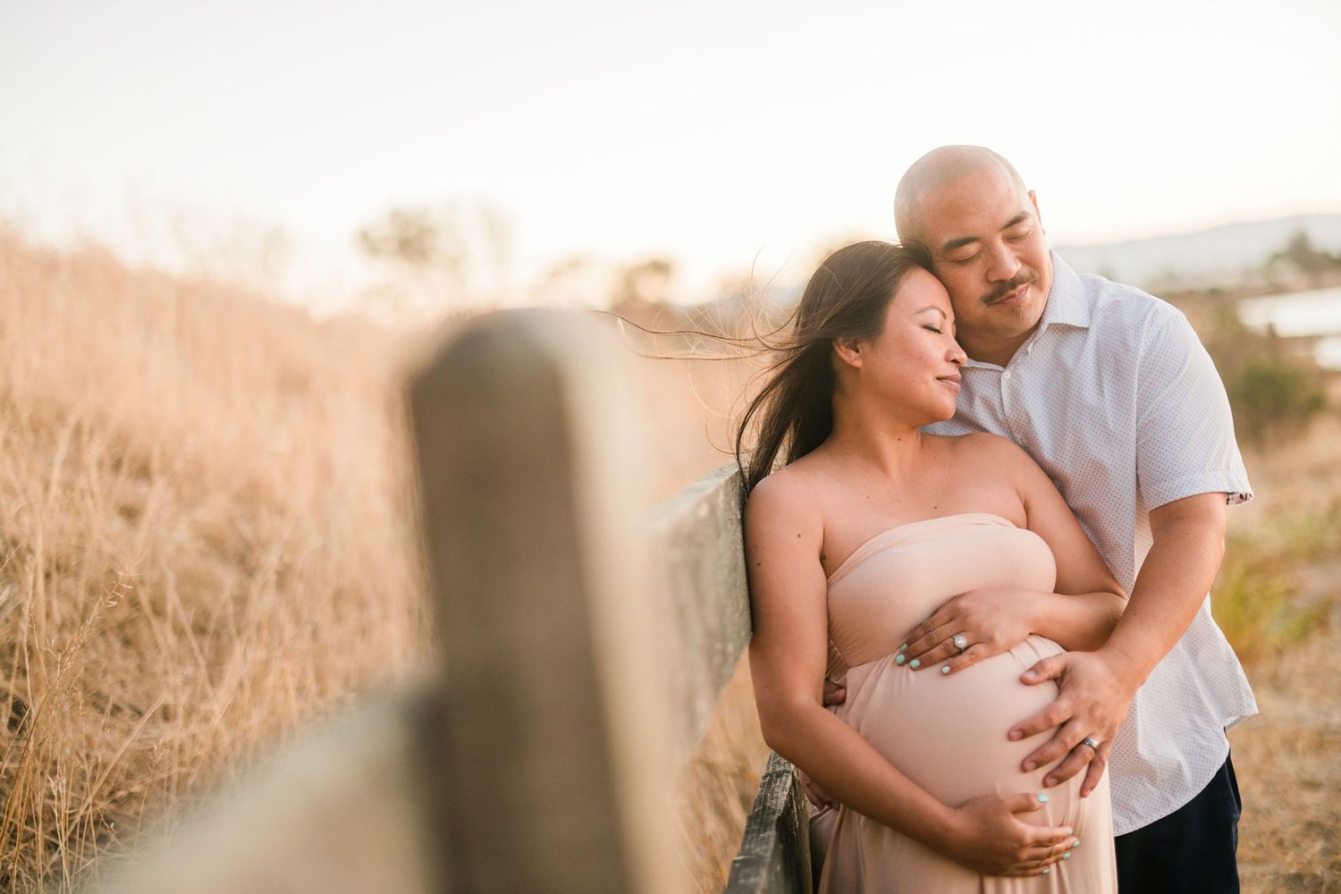 A couple shares a tender moment during a maternity photoshoot in a golden field.