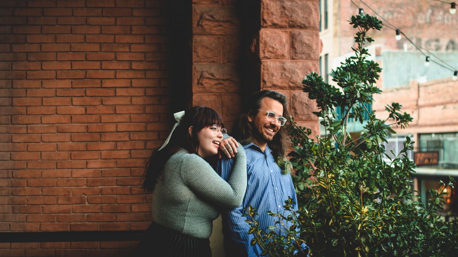 Two people sharing a candid laughing moment against a brick wall backdrop.