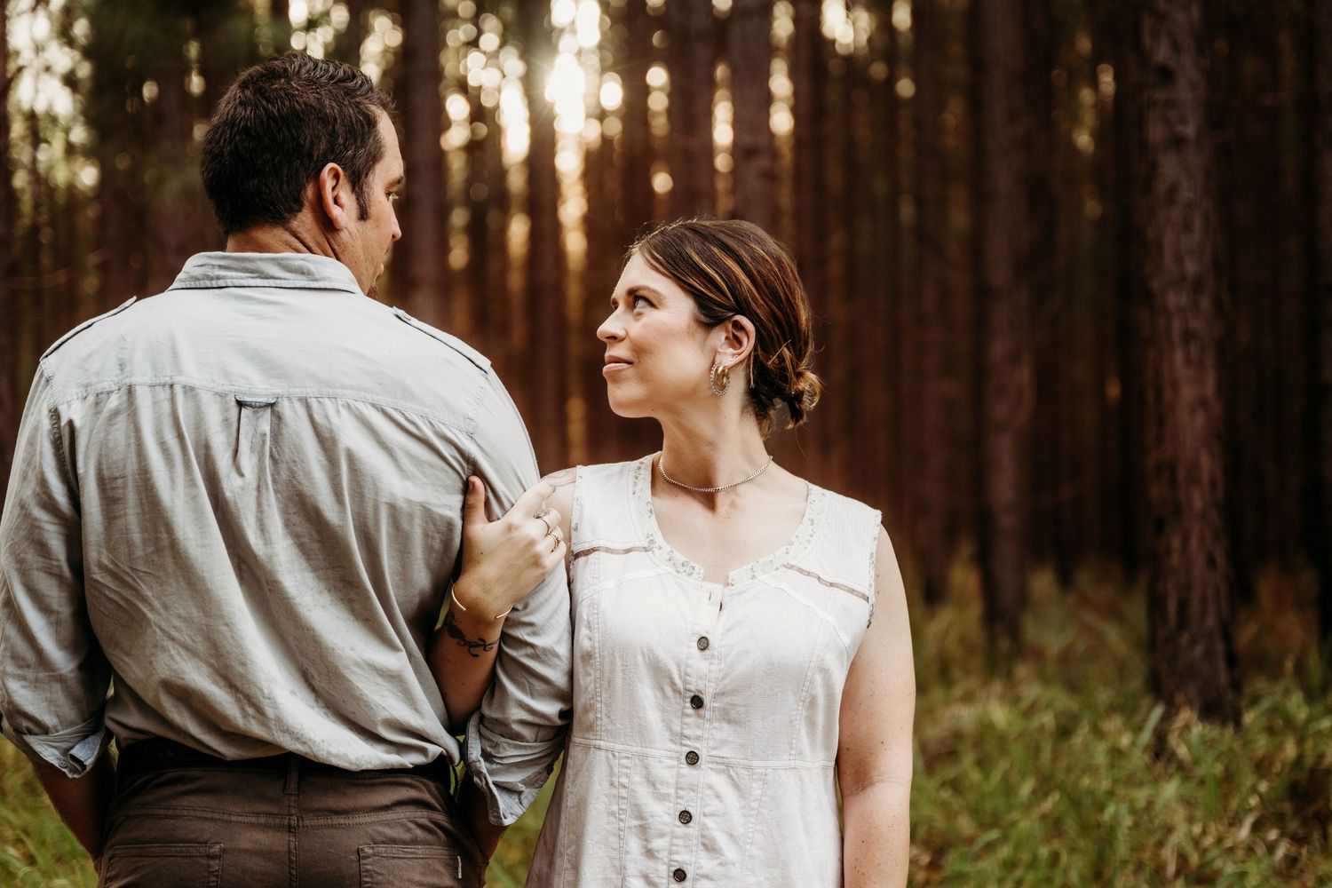 A couple in casual attire shares a tender moment in a sunlit forest.