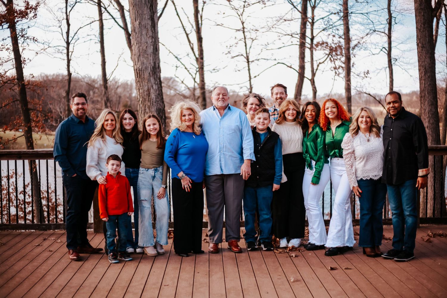 Large extended family group photo on wooden deck surrounded by winter trees.