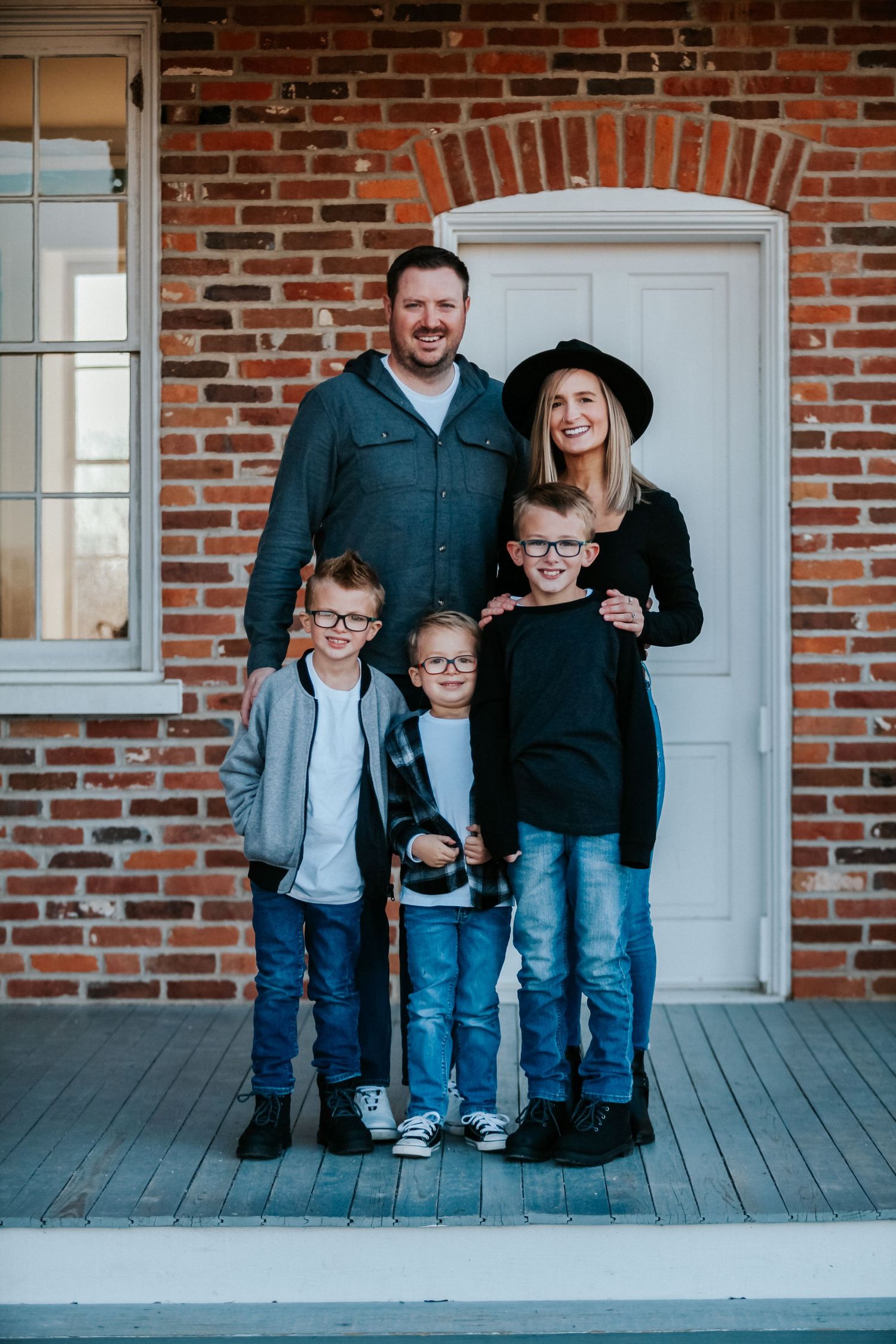 Family portrait on brick house porch with white door and coordinated outfits.