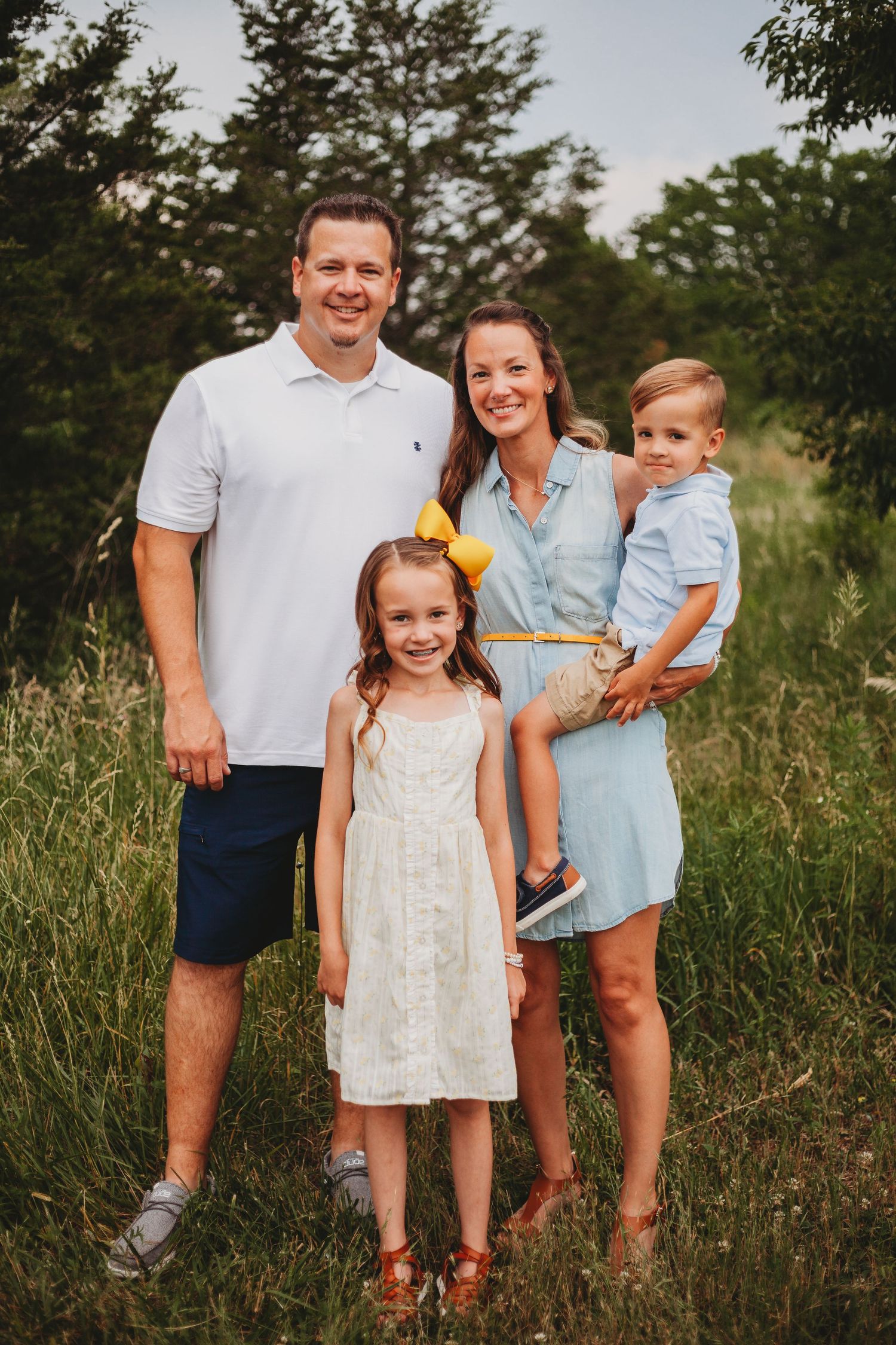 A family of four poses together outdoors in coordinated blue and white outfits against a natural background.
