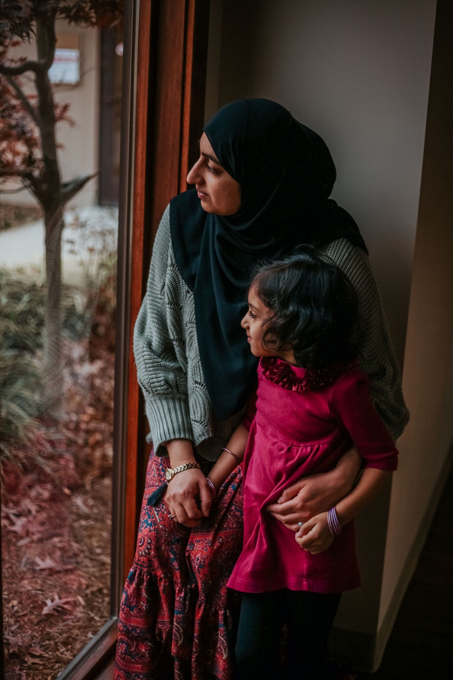 Intimate indoor family portrait with traditional dress and warm lighting by window.