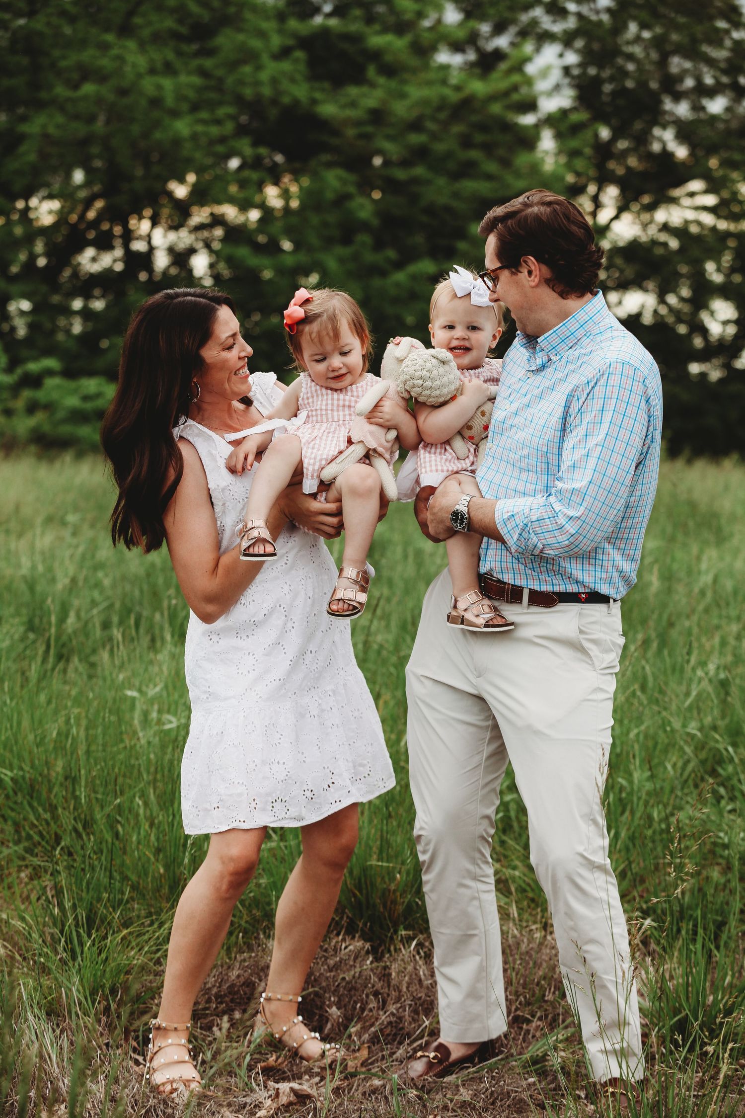Family sharing joyful laughter and embraces in tall grass during outdoor photo session.
