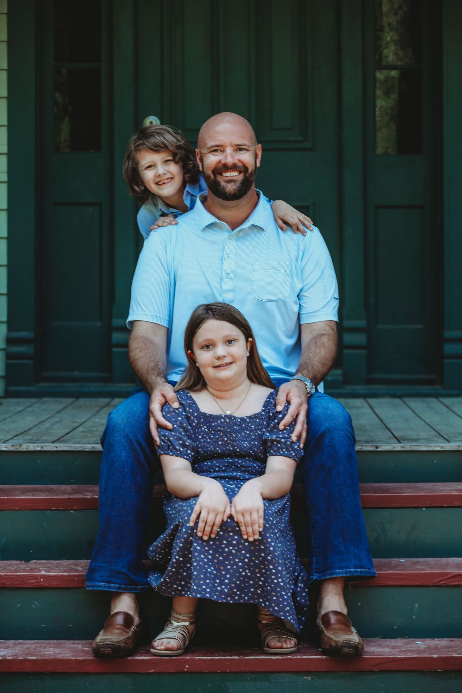 Family sitting together on wooden porch steps in casual attire during outdoor photo session.