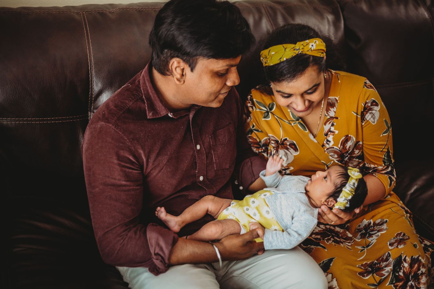 Family cuddling together on brown leather couch during indoor lifestyle session.
