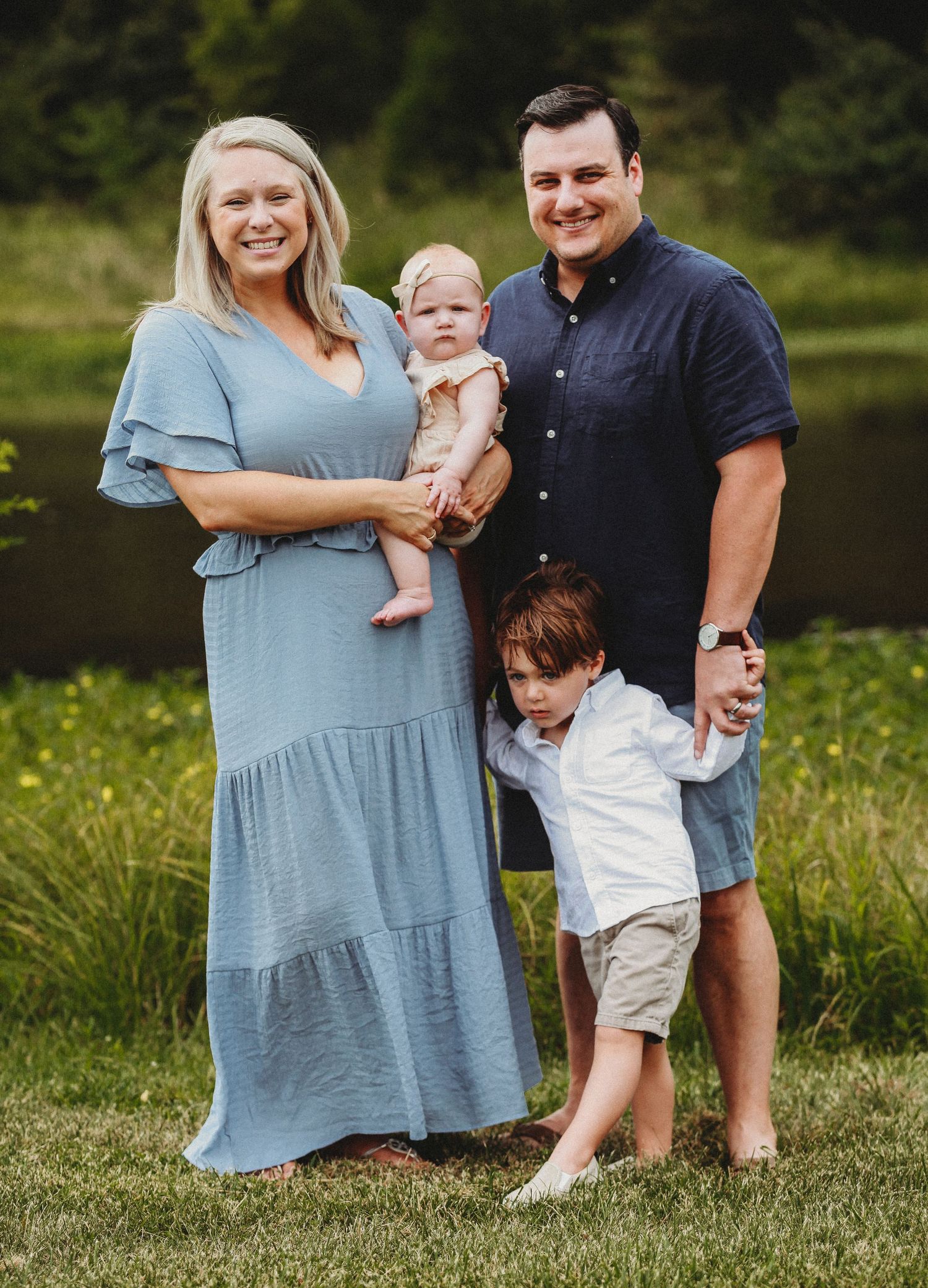 Family portrait by a lake with coordinating blue and neutral outfits.