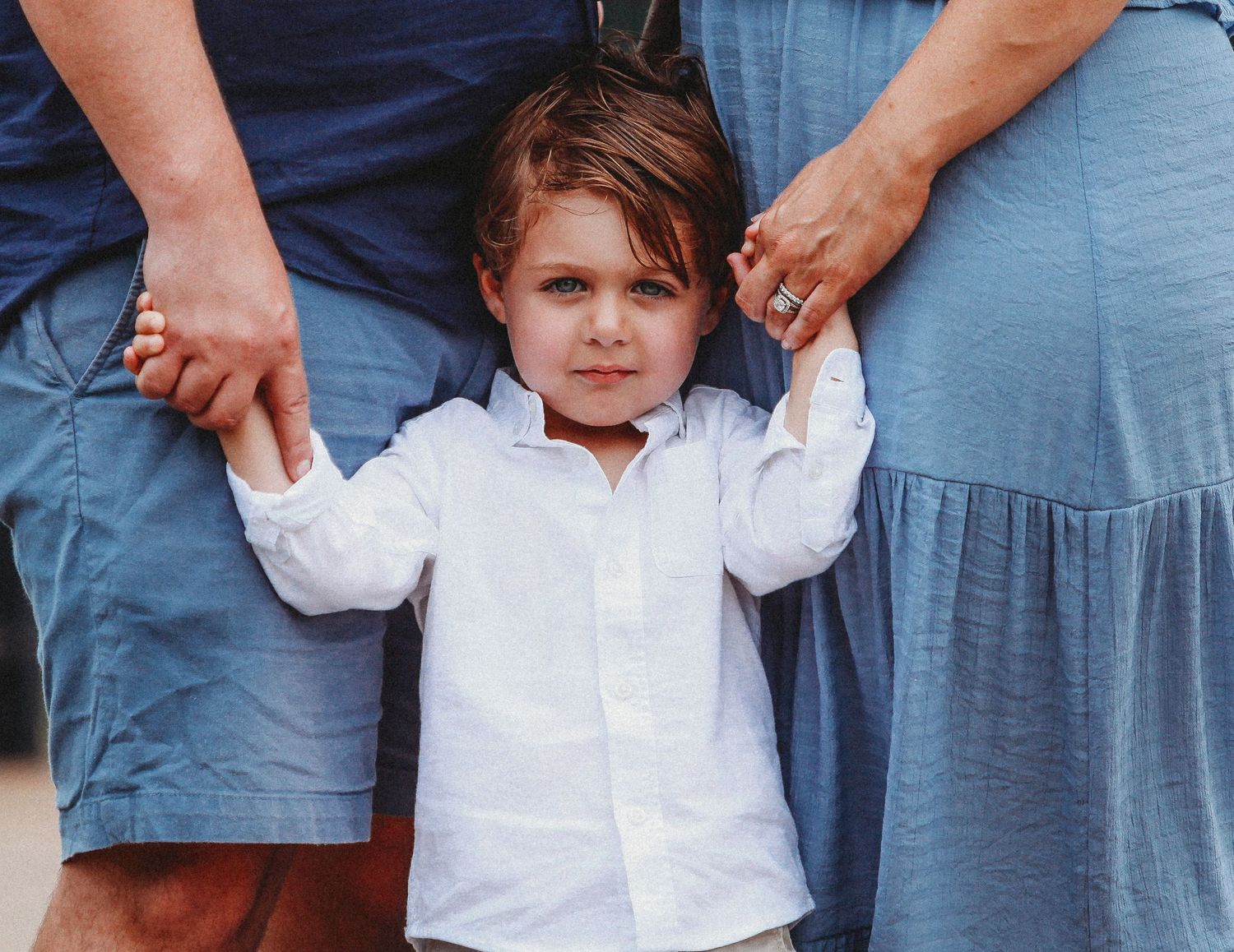 Young child in white shirt holding hands with adults in casual attire.