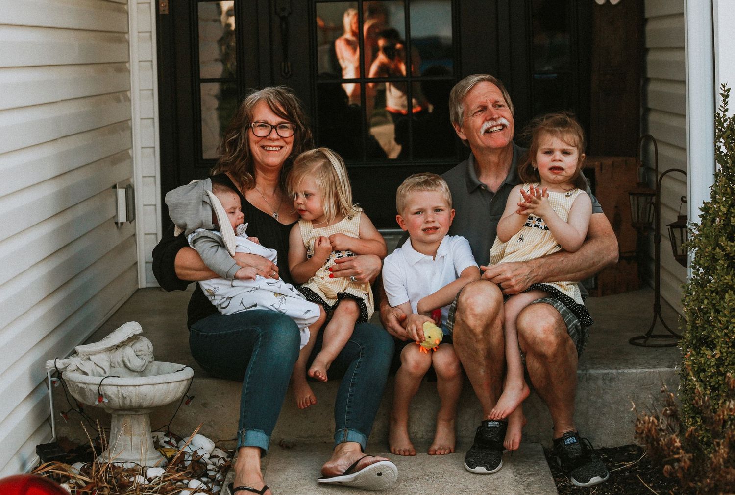 Family relaxing together on front porch steps of white house.