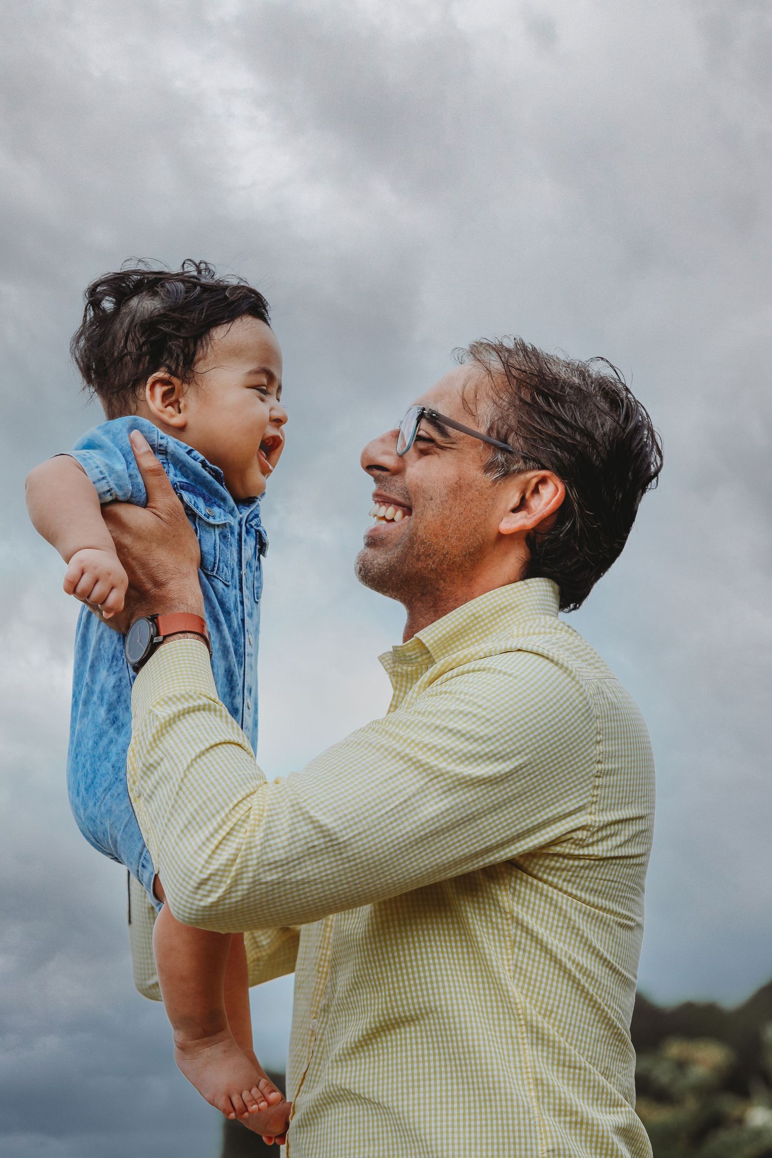 Joyful interaction between parent and child against dramatic cloudy sky.