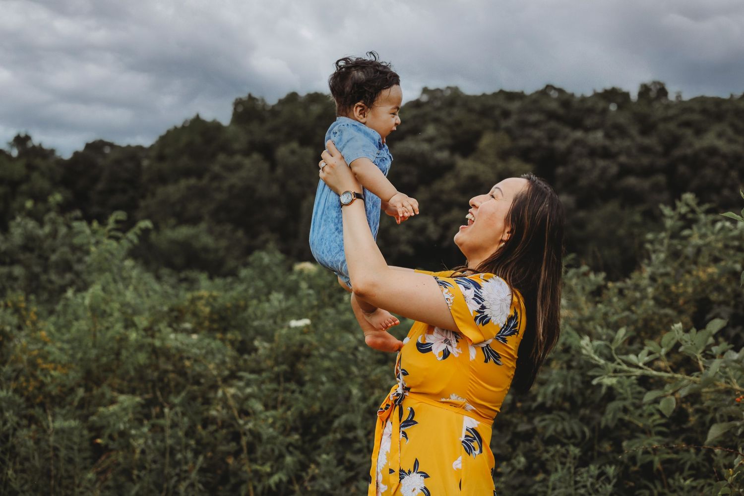 A tender moment captured outdoors as a parent lifts a child wearing blue against a cloudy backdrop.