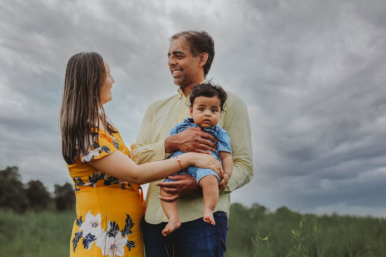 Family of three sharing an intimate moment outdoors against stormy skies.