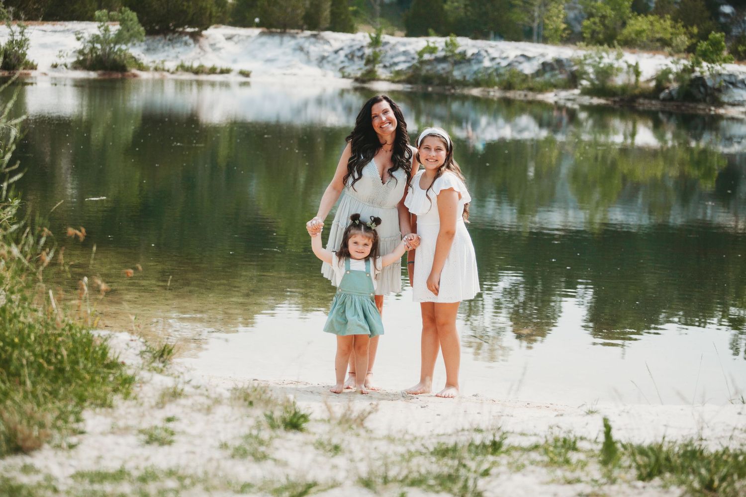 A family group poses together at the edge of a serene lake on a sunny day.