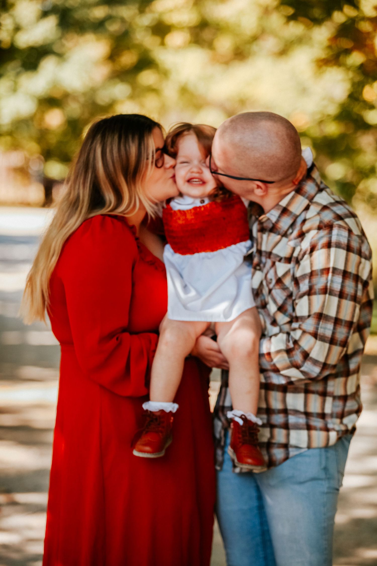 Intimate family moment sharing kisses and hugs while wearing red and plaid in outdoor setting.