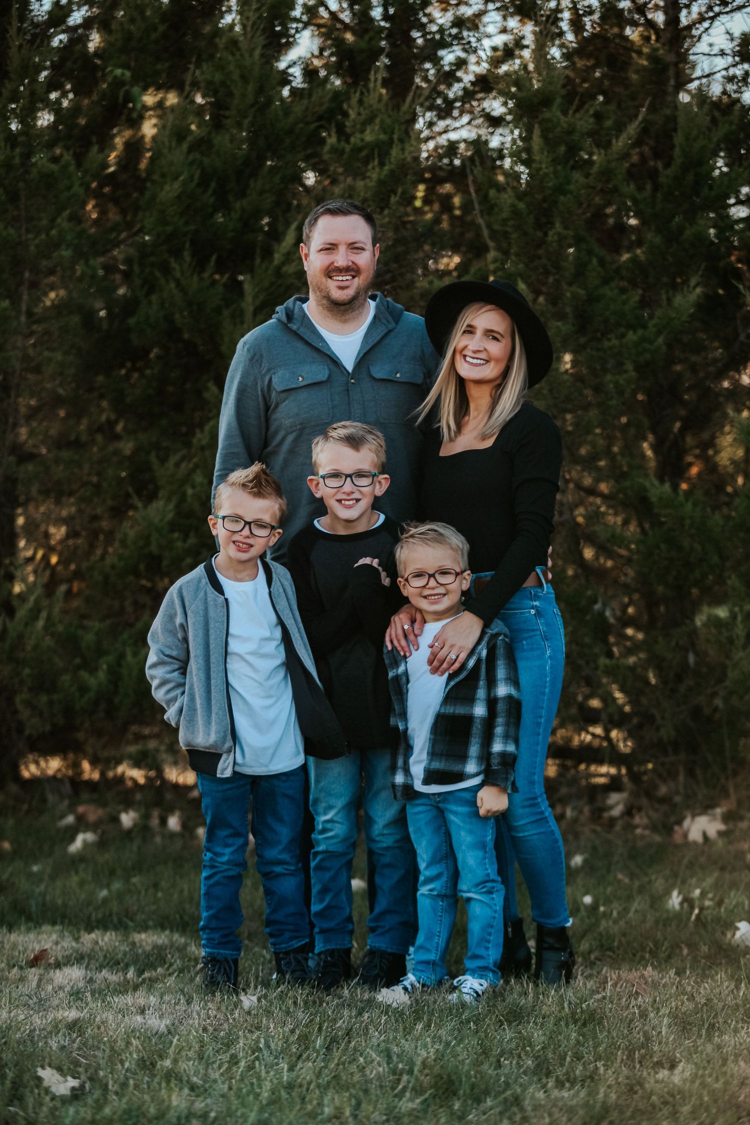 Family portrait session in casual attire against a natural wooded backdrop during golden hour.