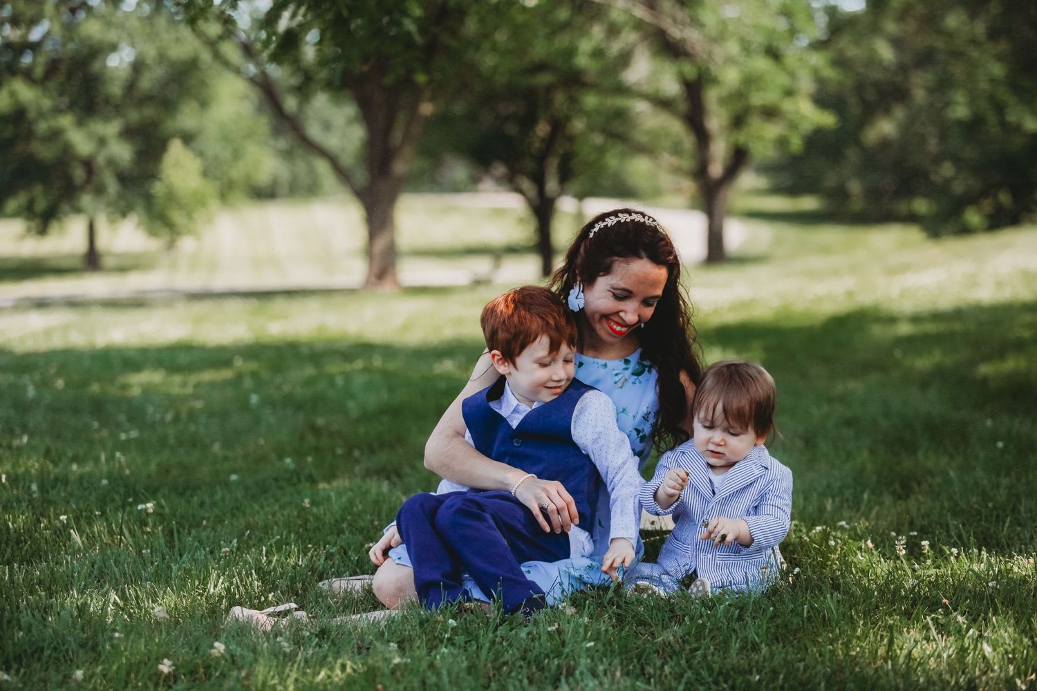 Three people sit together on lush green grass in a sunny park setting.