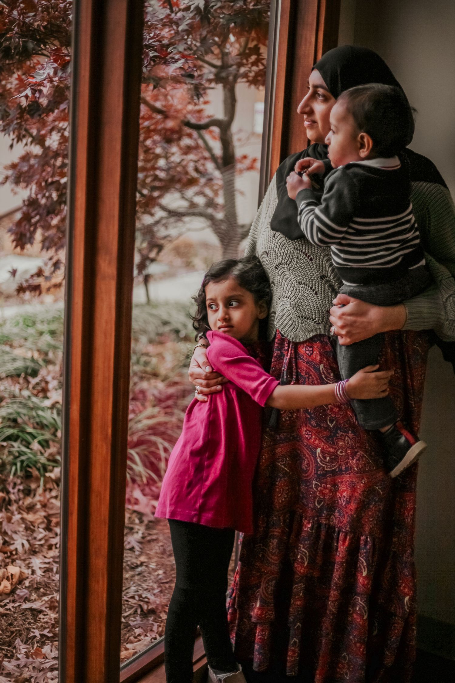 Family moment captured by window with child in bright pink dress.