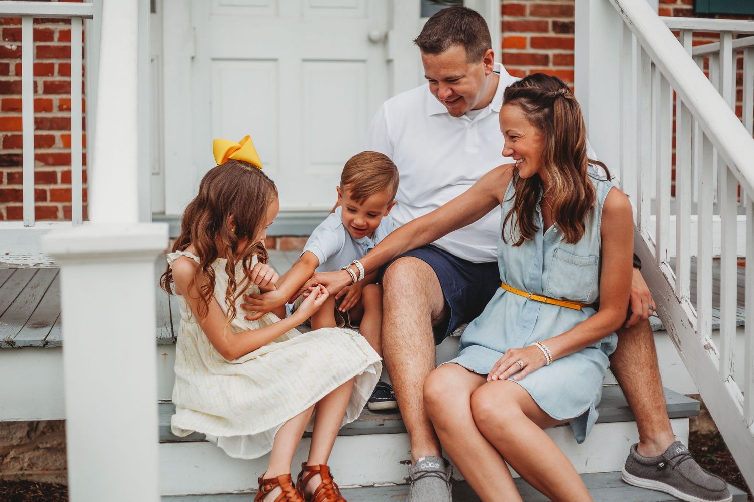 A family shares a candid moment together while sitting on white porch steps.