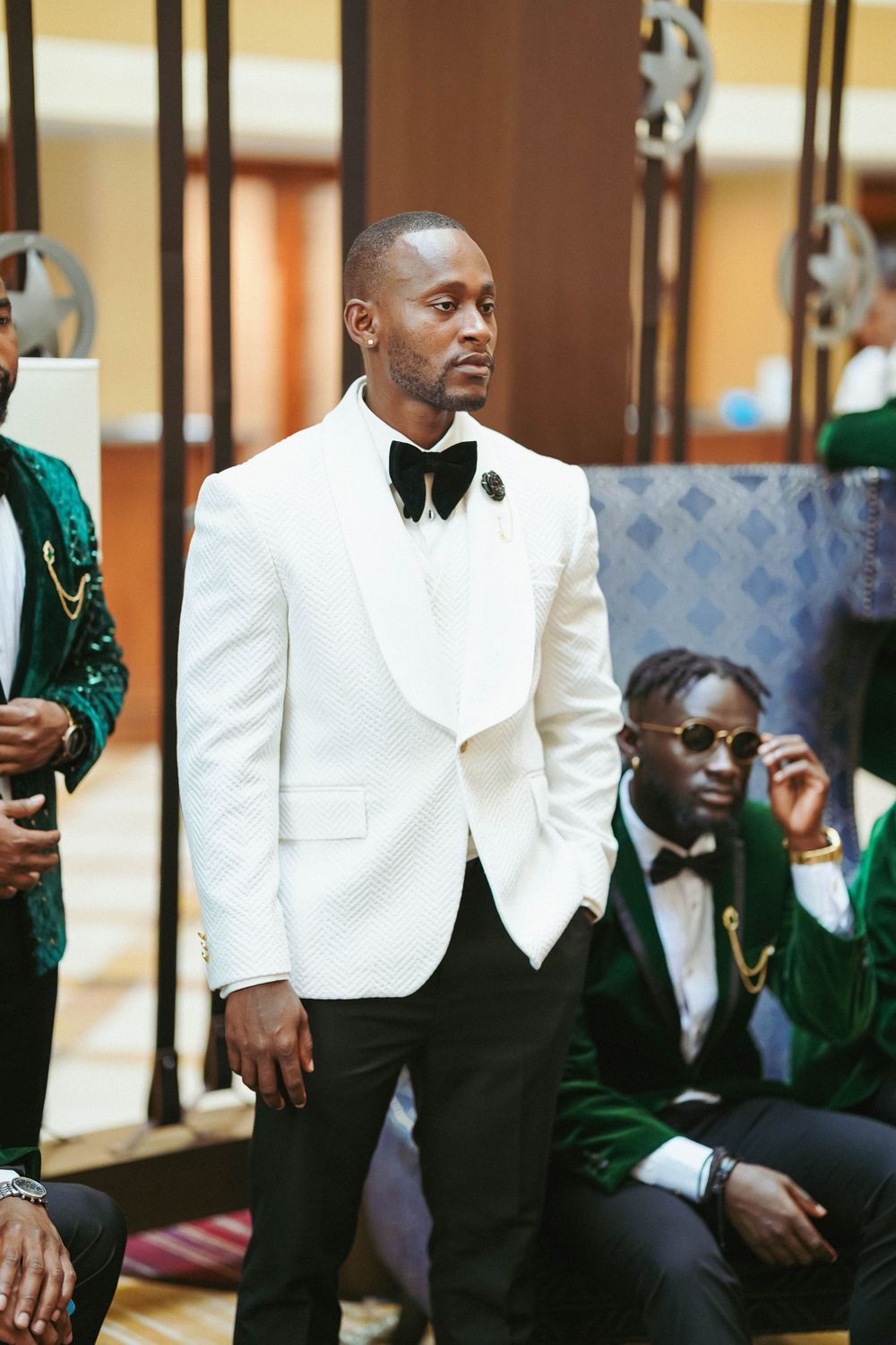 Wedding party in mix of white and green velvet tuxedos pose together in formal venue.