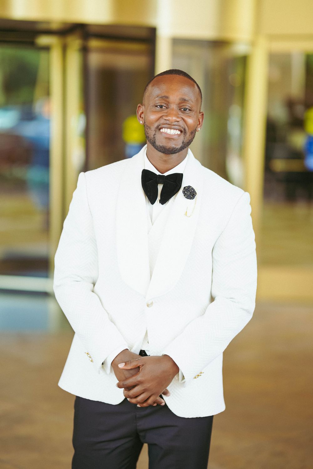 Well-dressed man in white tuxedo shows joyful expression while posing in an elegant hallway.