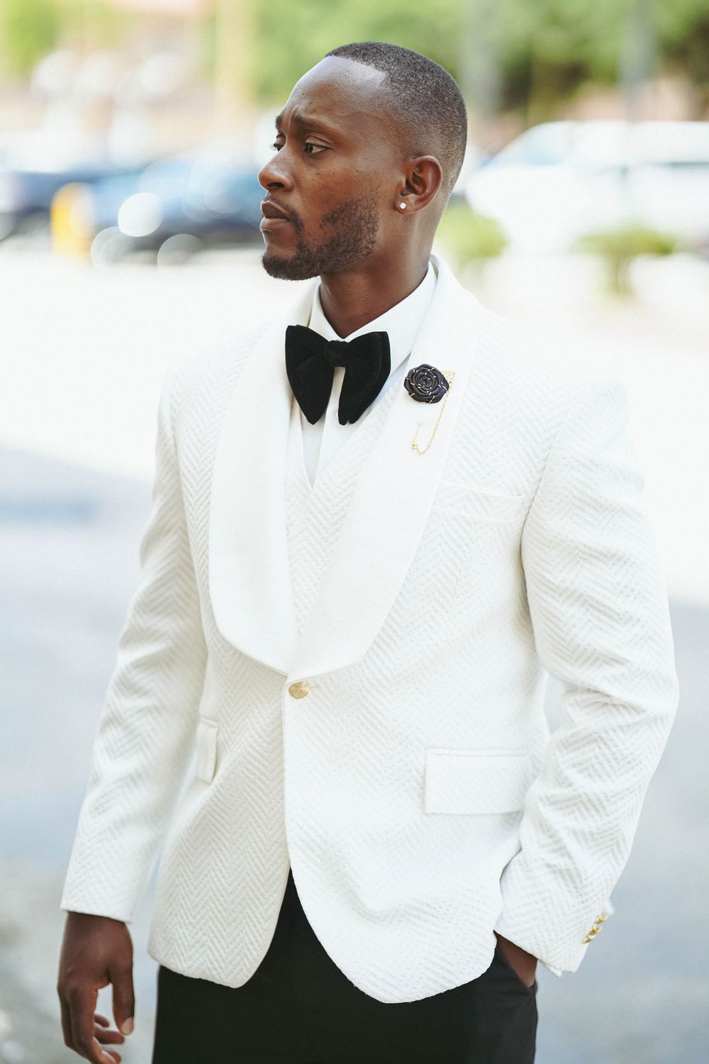 Groom in crisp white textured dinner jacket and black bow tie poses outdoors.