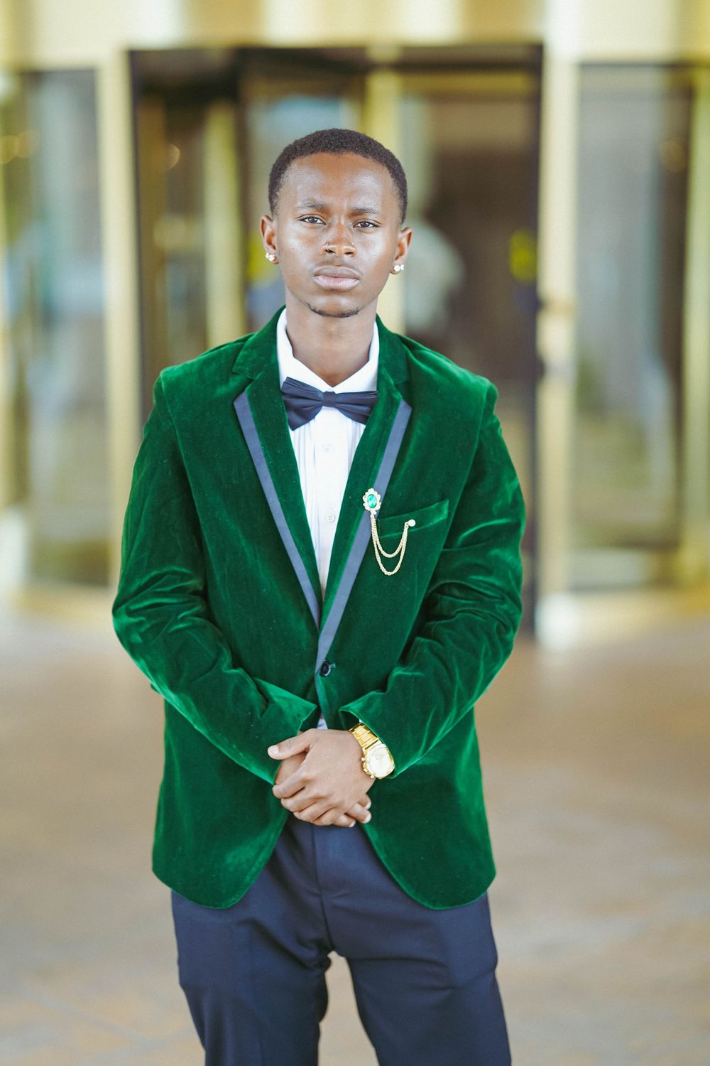 Gentleman in luxurious green velvet jacket and bow tie poses confidently in formal setting.