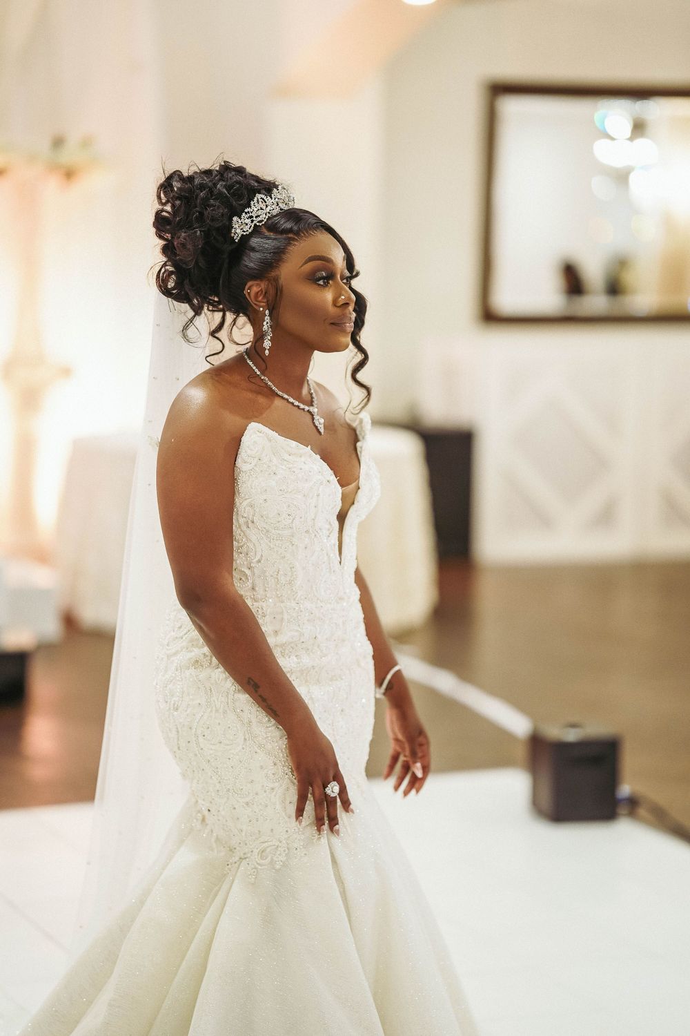 Bride in elegant fitted lace gown with plunging neckline and tiara poses during wedding portraits.
