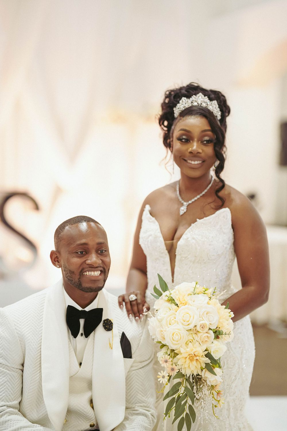 Wedding portrait showcasing happy couple with white floral bouquet against light backdrop.