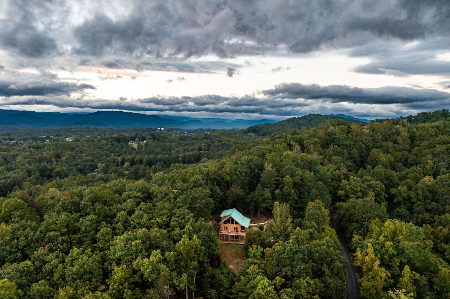 Aerial view of lush green forest landscape with a small house nestled among rolling hills.
