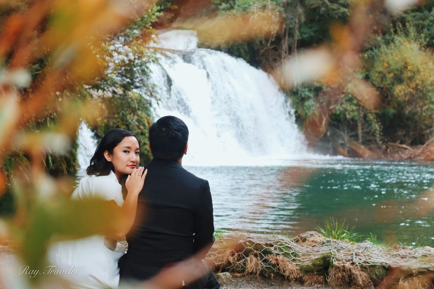Scenic waterfall view framed by autumn foliage with couple in foreground.