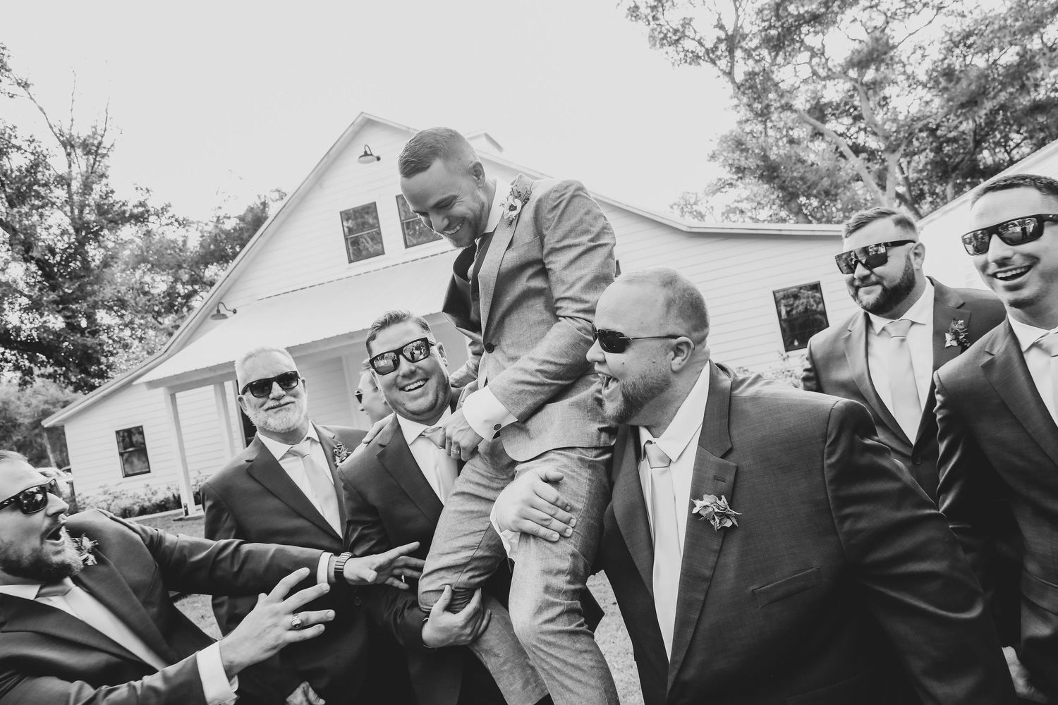 A black and white photo showing groomsmen lifting and carrying someone during wedding celebrations.