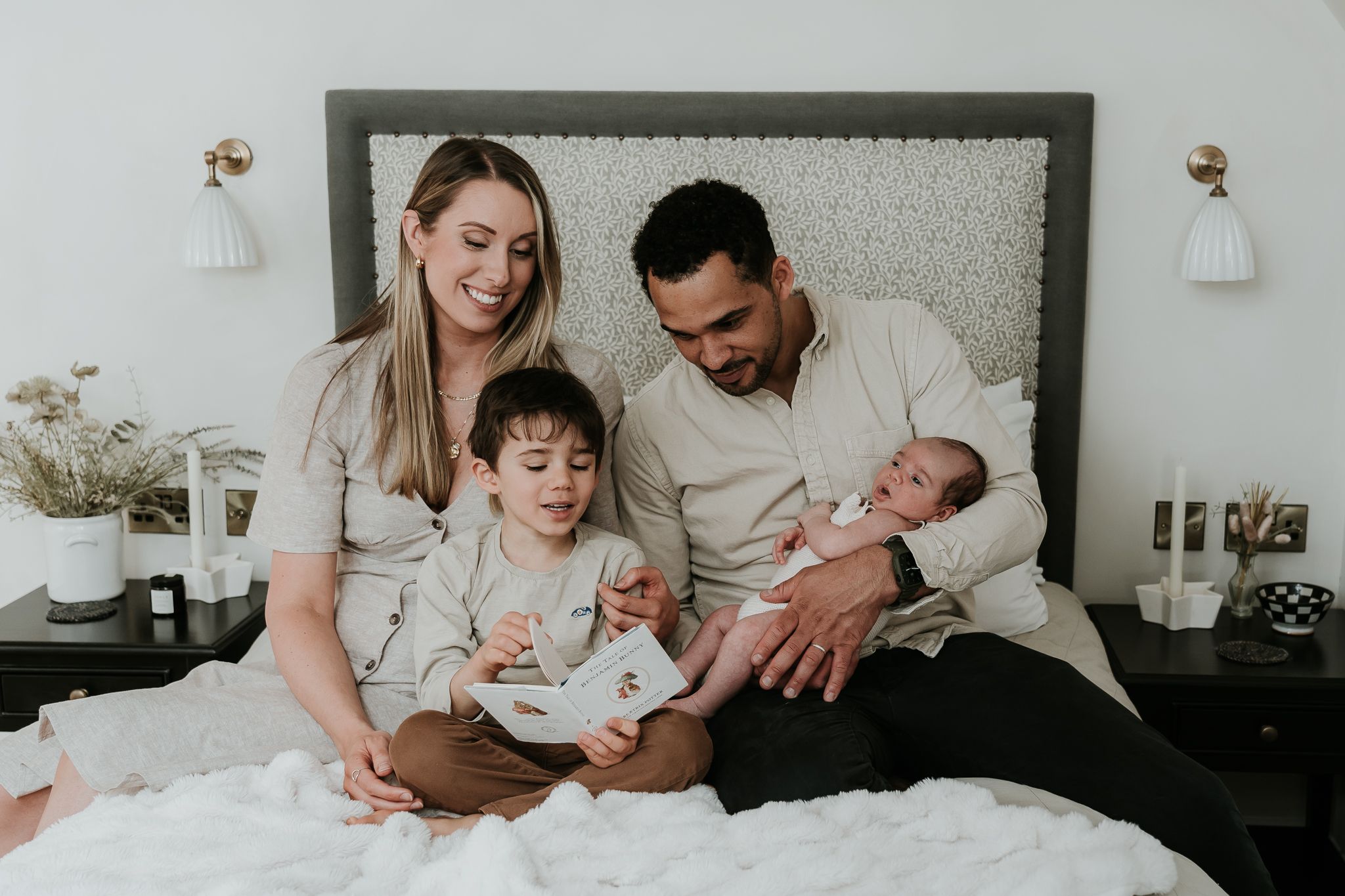 A family relaxes together on a white bed with pillows and blankets.