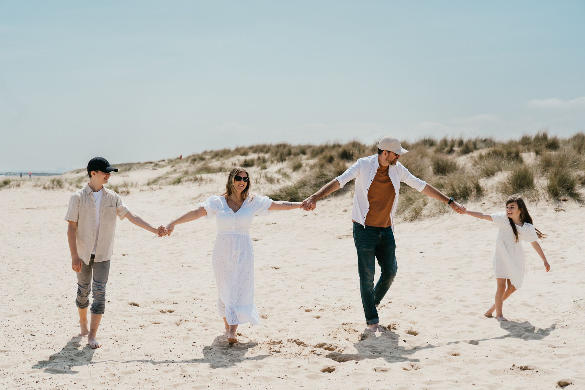 Family holding hands while walking on sandy beach dunes during a sunny day.