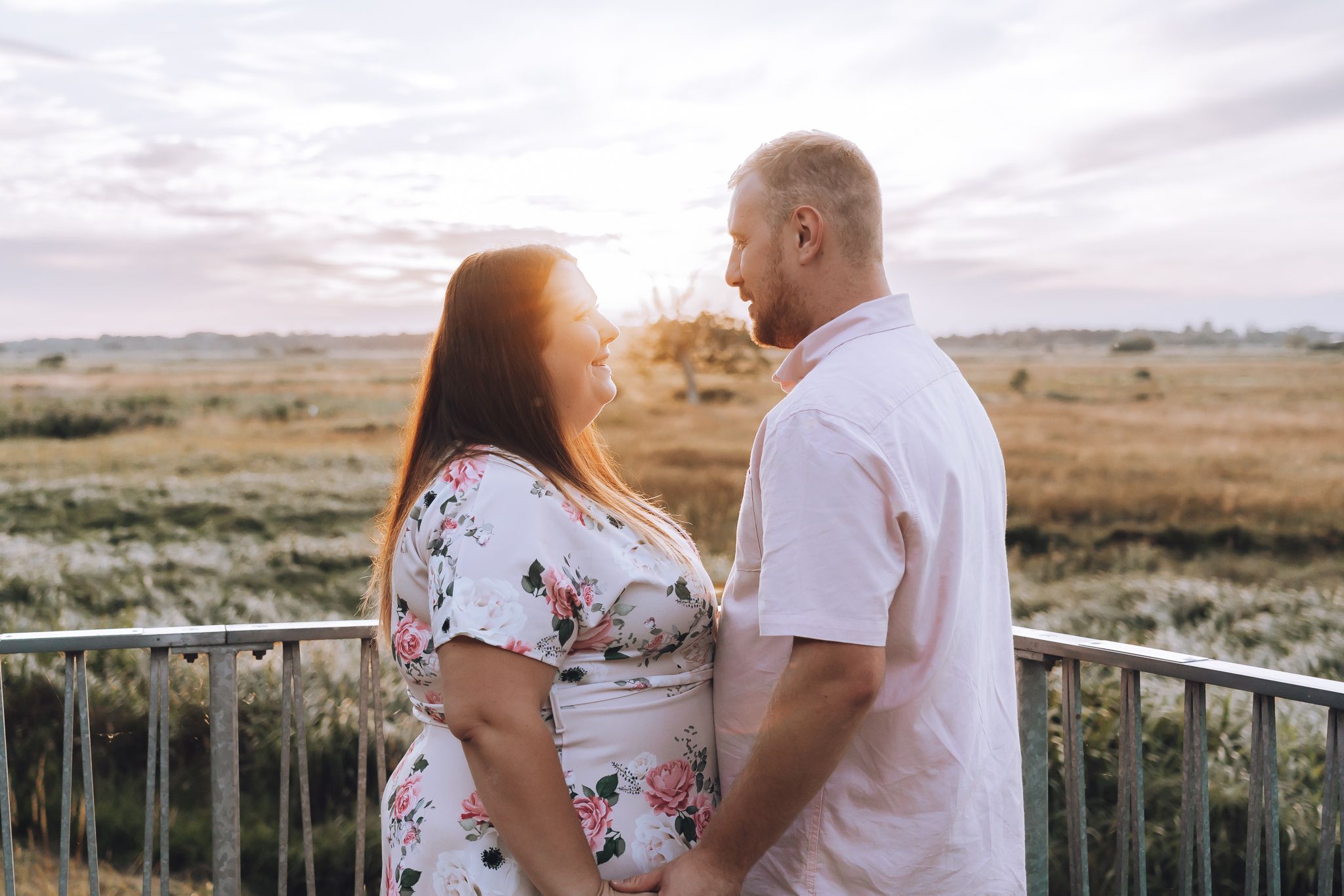 Romantic couple standing together on balcony overlooking scenic landscape at sunset.