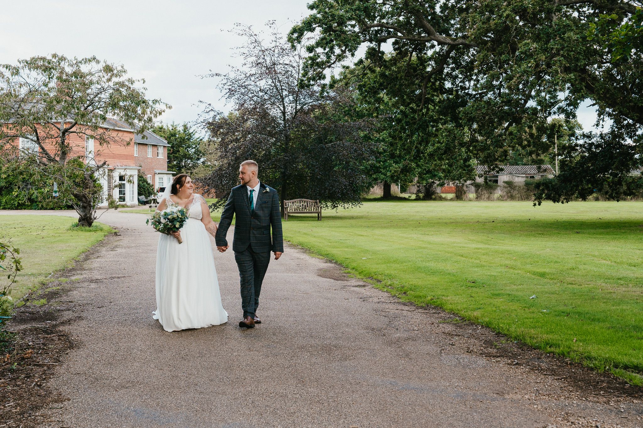 Newlyweds walking down tree-lined path at elegant estate venue.