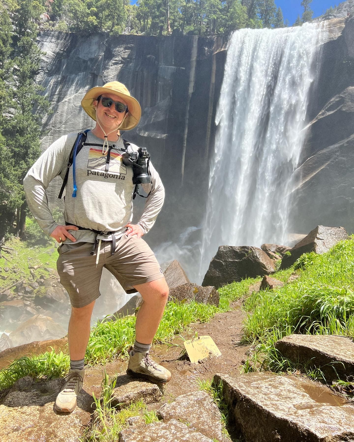 Hiker poses in outdoor gear near spectacular waterfall in scenic mountain landscape.