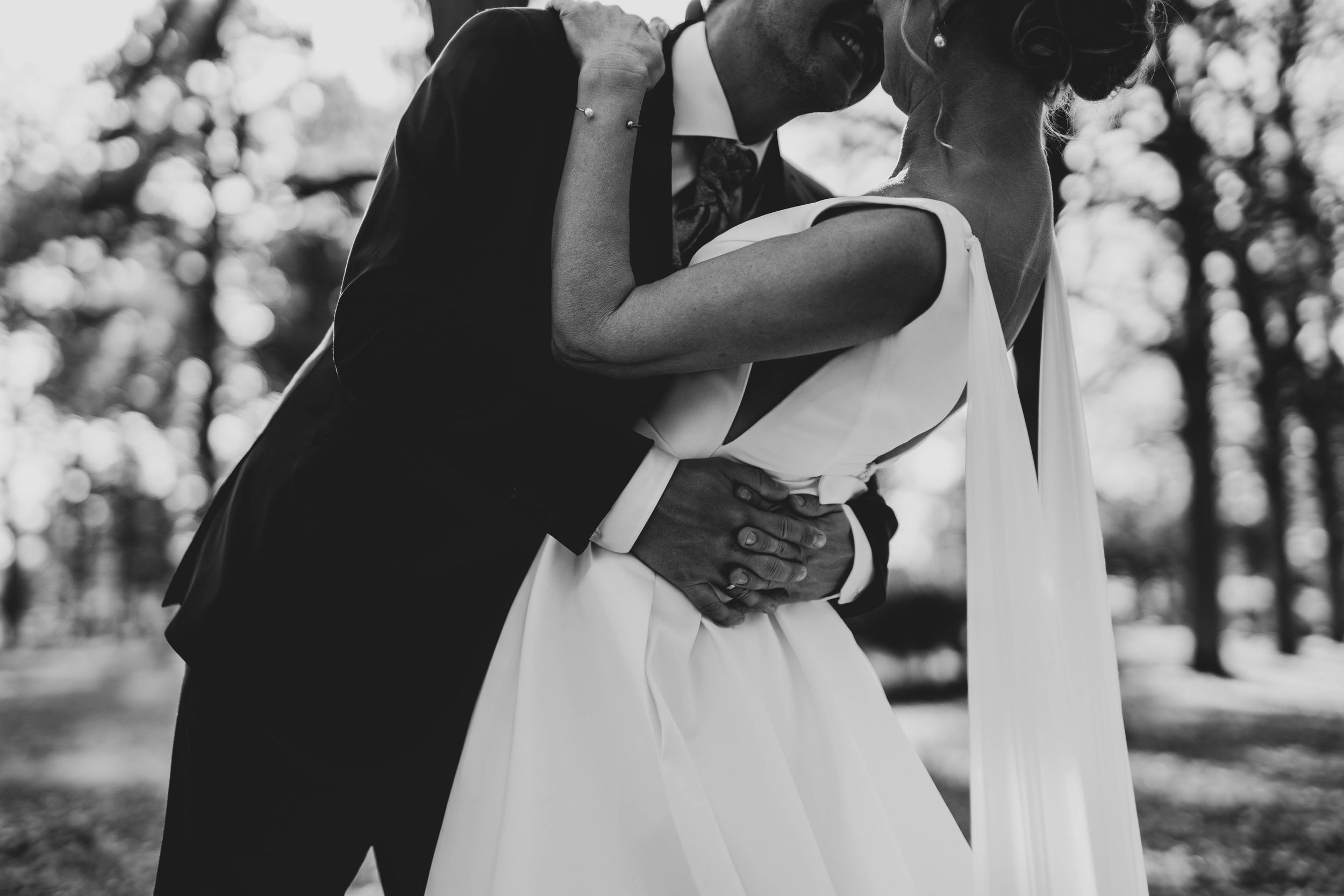 Black and white photograph of romantic wedding embrace in park setting.