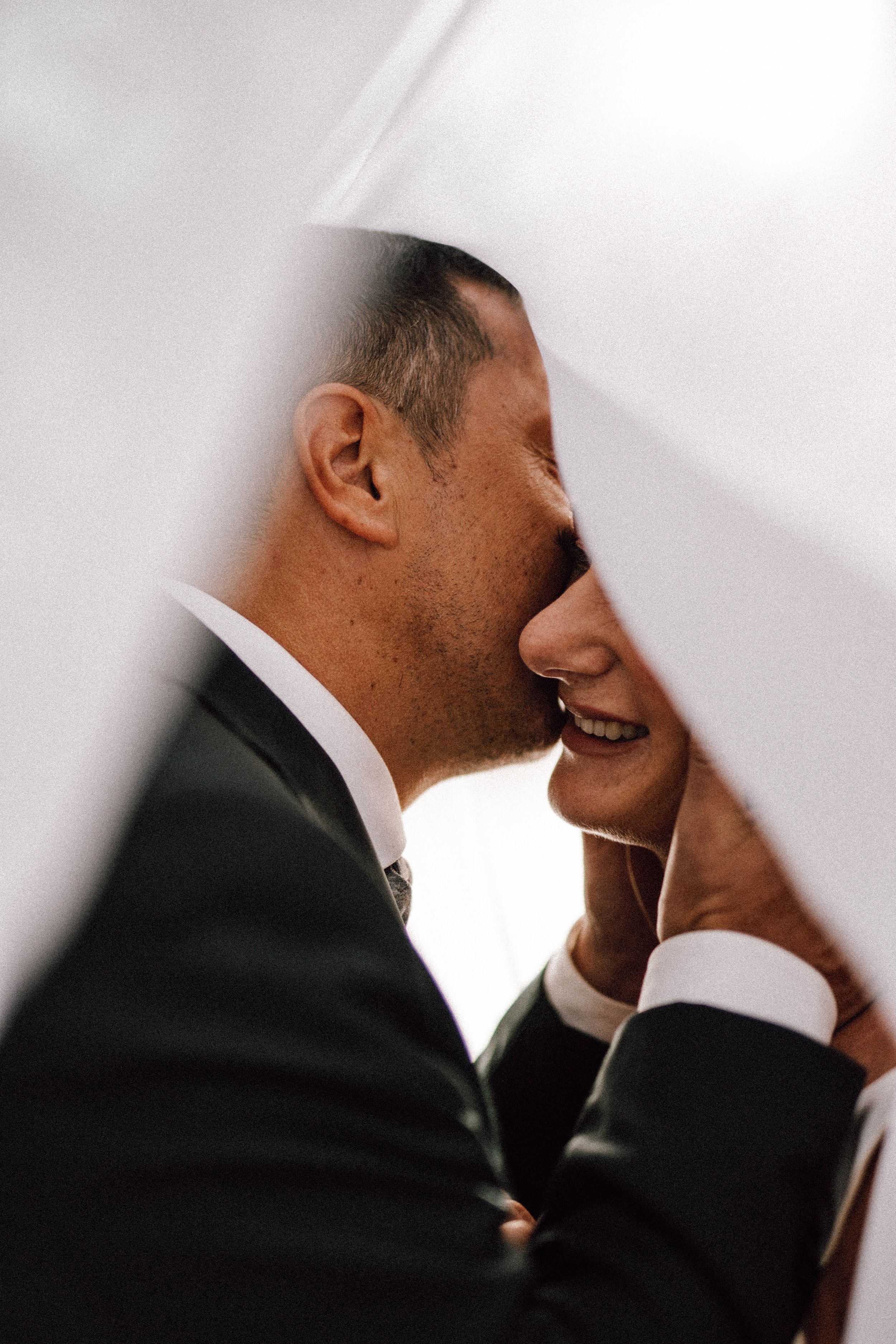 Intimate close-up of romantic moment through white veil during wedding ceremony.