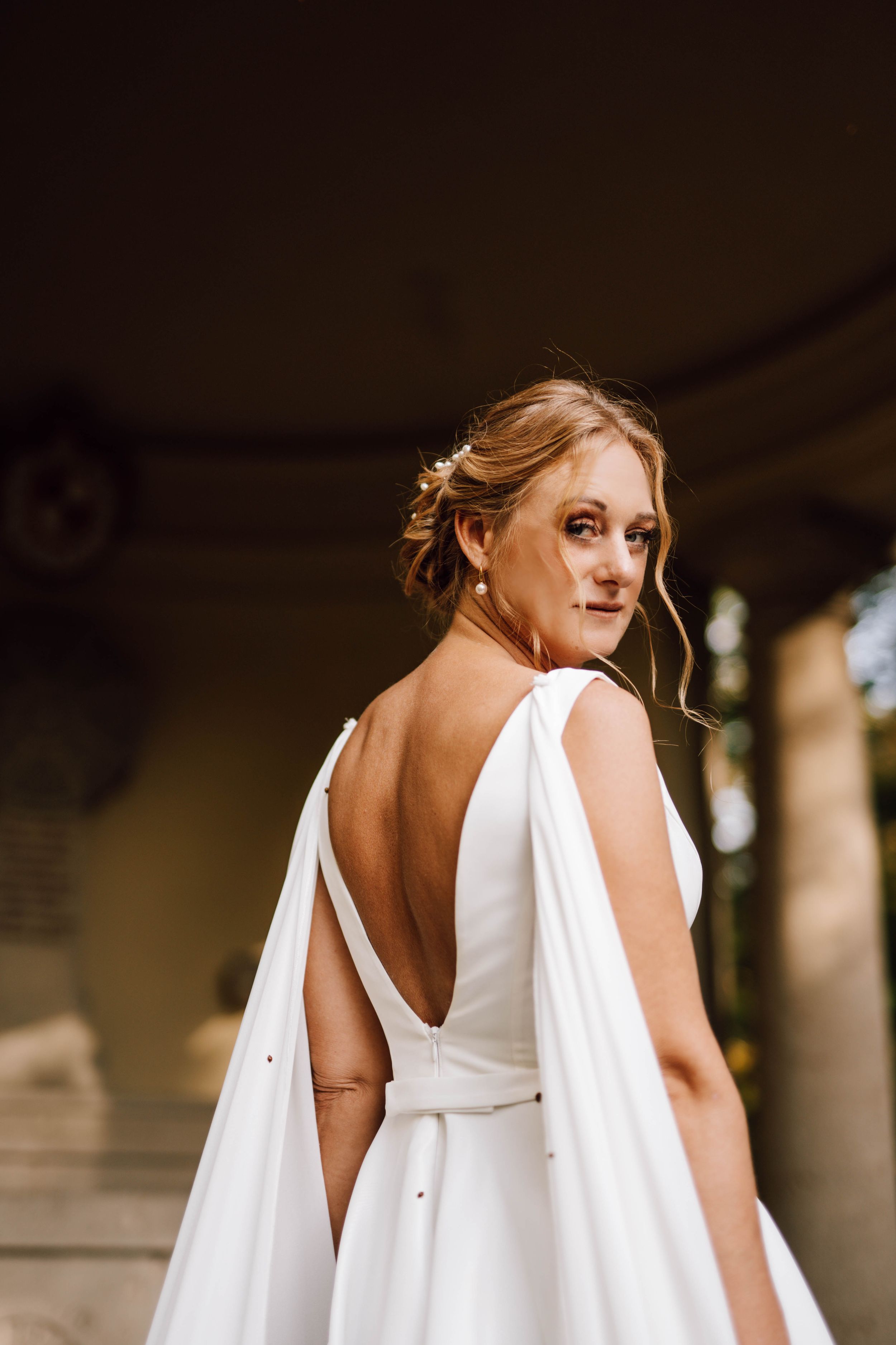 Elegant white wedding dress with flowing cape details photographed in natural light.