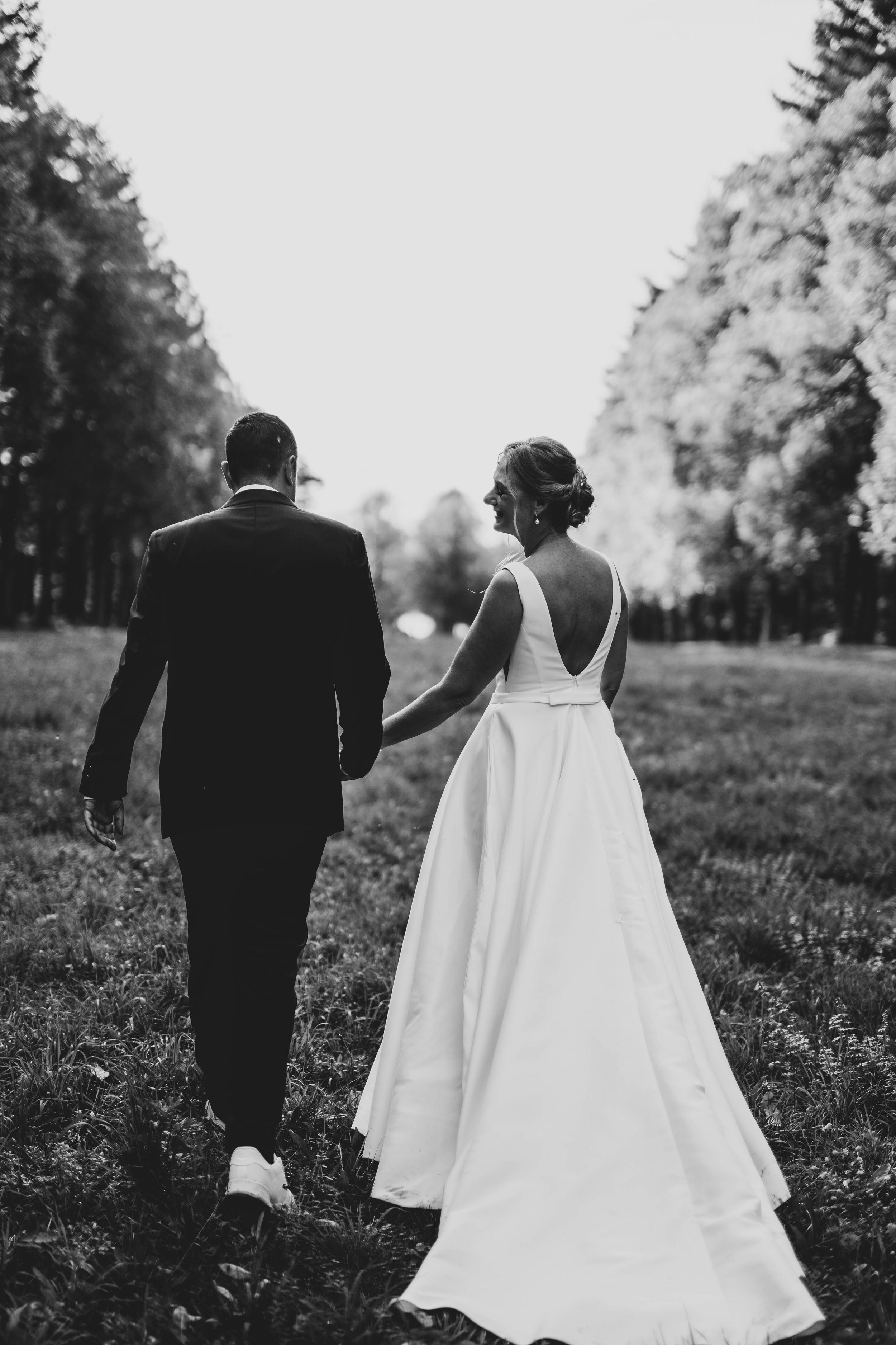 Black and white portrait of newlyweds walking through a meadow.