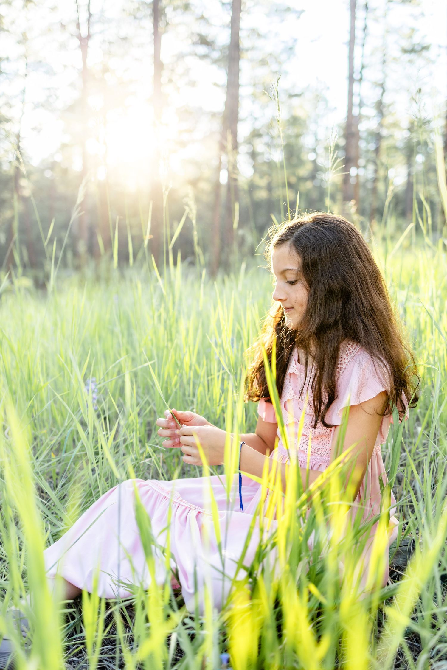 Young girl plays with a flower while sitting in the grass during their family session in Colorado Springs.