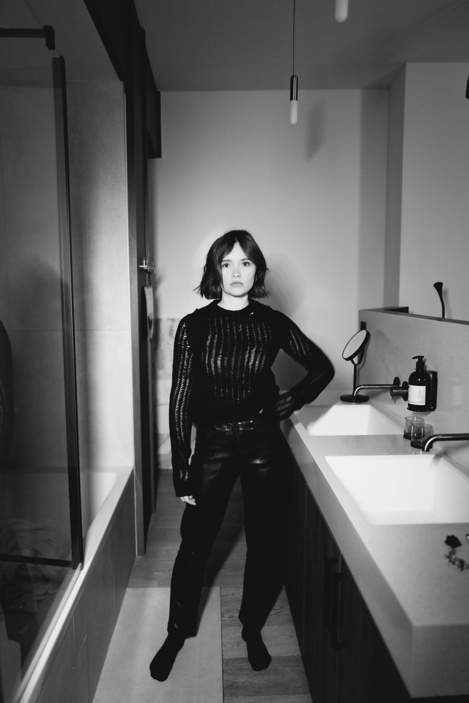 Modern interior photoshoot featuring dark clothing and minimalist white bathroom setting.