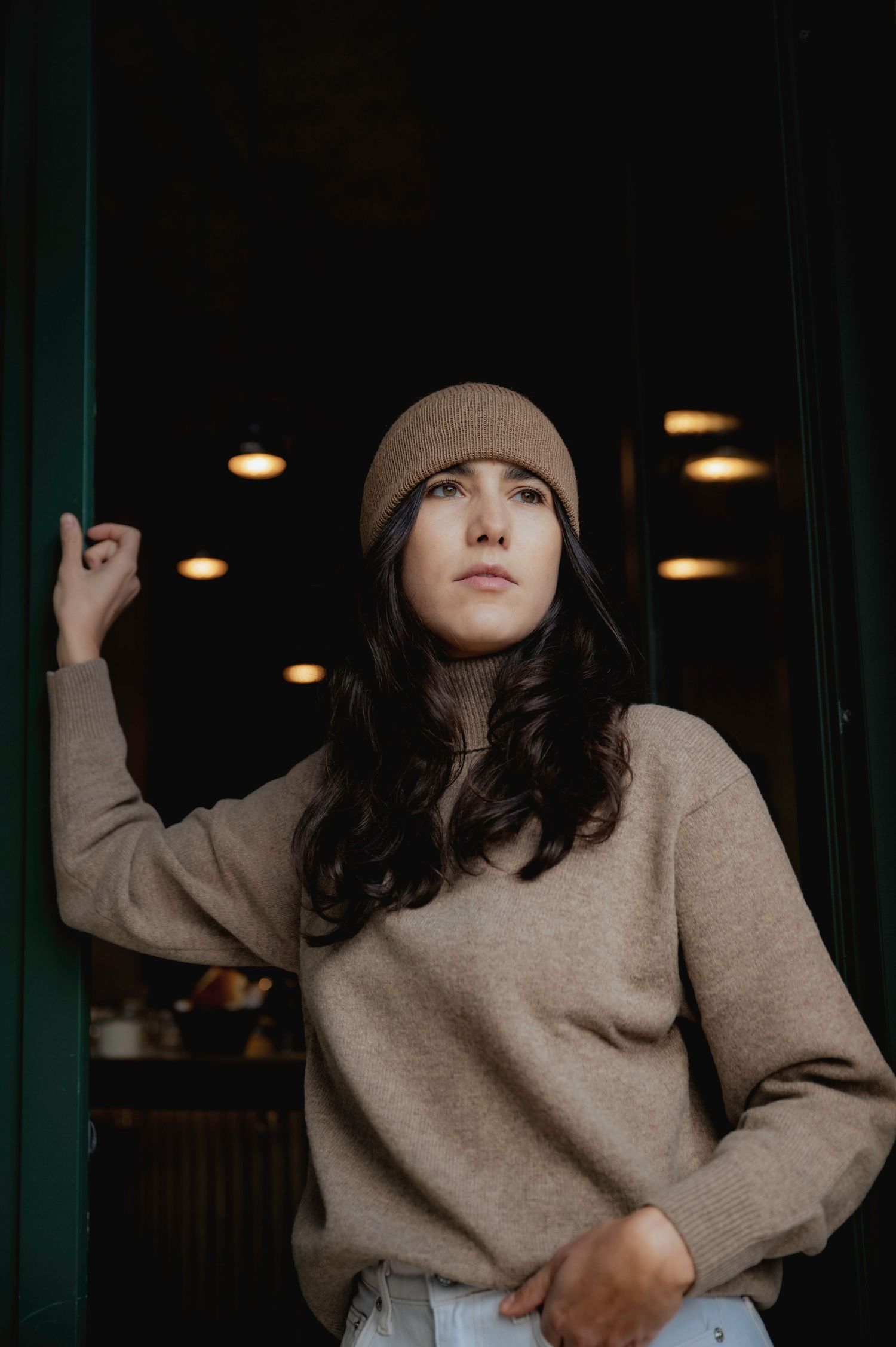 Moody indoor portraits featuring a beige sweater in dim lighting.