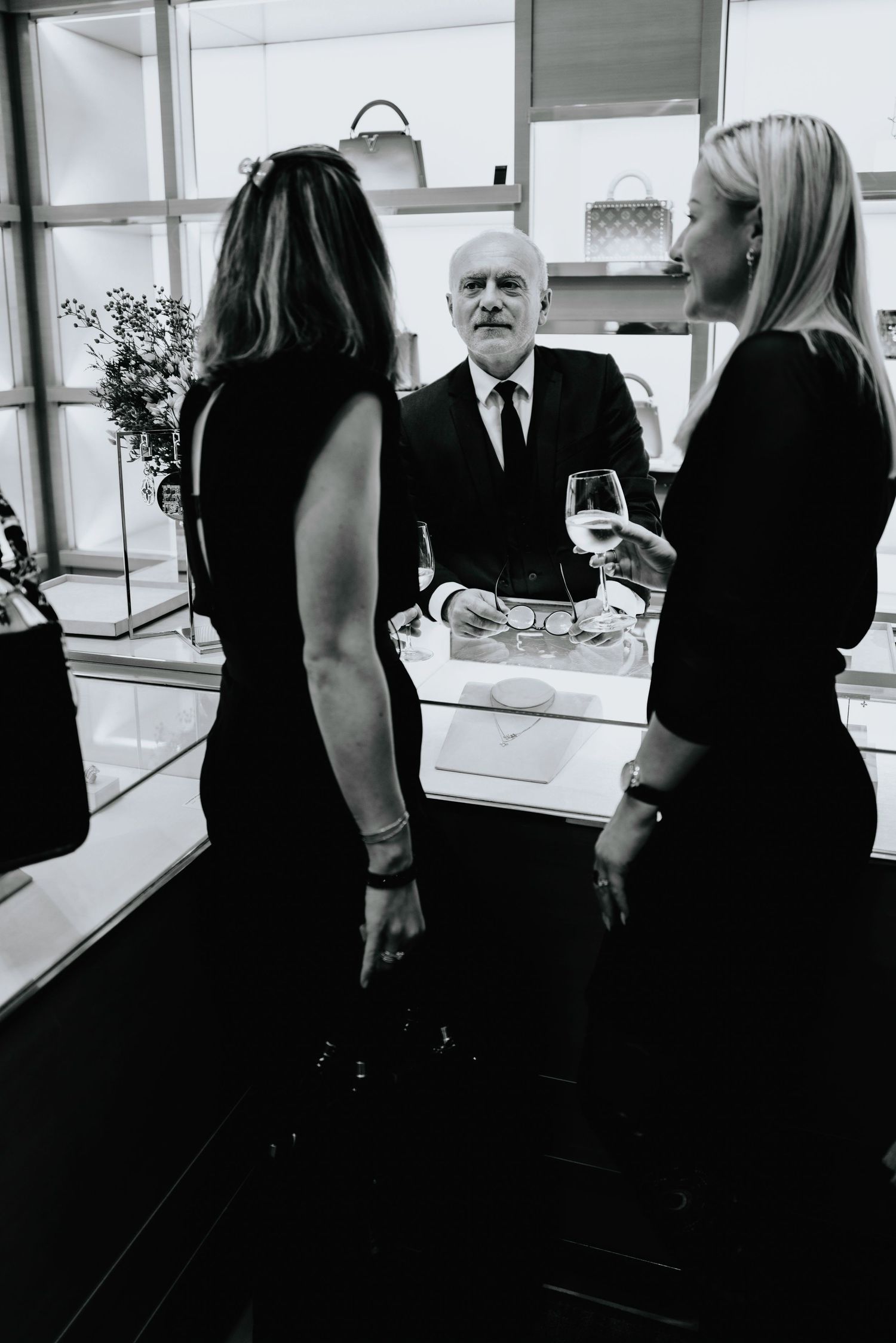 Black and white candid scene of people gathered around a counter in formal attire.