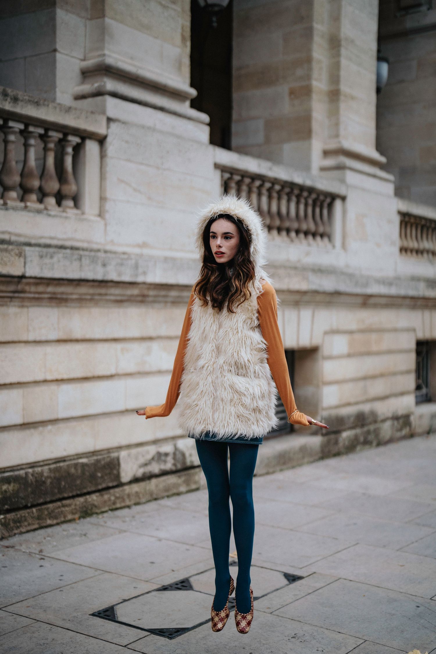 Fashion photography showcasing furry cream vest and casual wear against classic architecture.