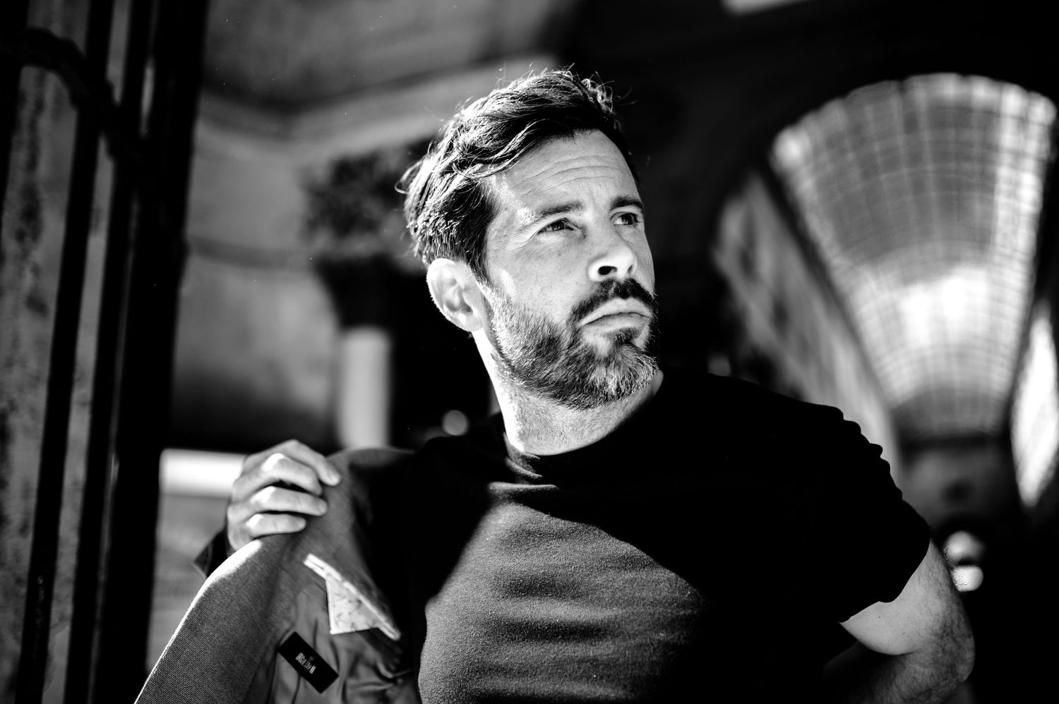 Dramatic black and white portrait of man in dark shirt with contemplative expression.