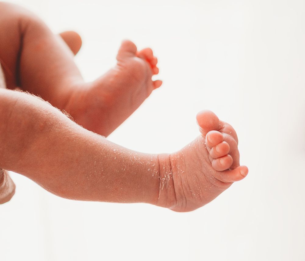 Close-up view of tiny baby feet and legs against a white background.