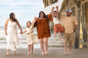 Family enjoying a joyful moment walking together under a wooden pier by the beach.
