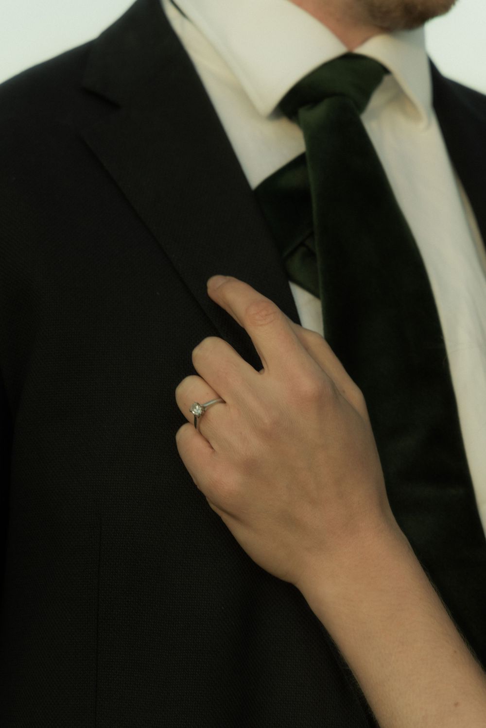 Close-up of hands adjusting a black tie against a formal suit jacket.