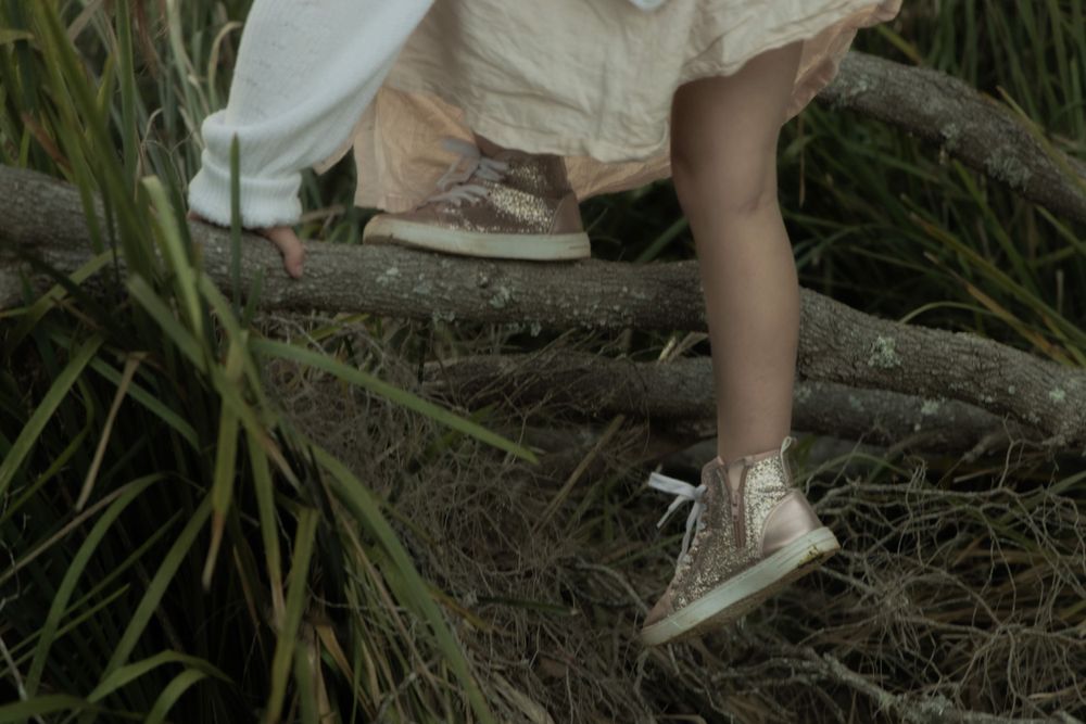 Close-up of Childs feet and dress hem resting on natural wood elements in an outdoor setting.